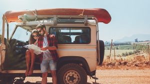 Young couple stopping on country road and looking at the map for directions. Man and woman on a road trip in countryside on a summer day.